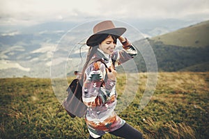 travel and wanderlust concept. stylish traveler hipster girl holding hat, with backpack and windy hair, walking in mountains in c