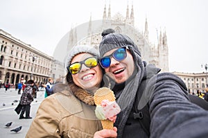 Travel in winter and Italy concept - Happy young couple take selfie photo with ice-cream in front of Milan Duomo