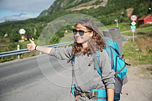 Travel woman hitchhiking. Backpacker on road. Happy smiling gorl with big backpack, Norway