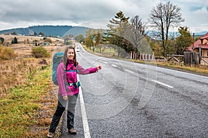 Travel woman hitchhiking. Beautiful young female hitchhiker by the road during mountain trip