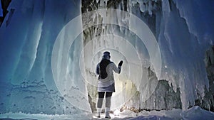 Travel woman on ice cave of Lake Baikal. Trip to winter island. Girl backpacker is walking of ice grot. Traveler looks