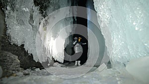 Travel woman on ice cave of Lake Baikal. Trip to winter island. Girl backpacker is walking of ice grot. Traveler looks