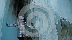 Travel woman on ice cave of Lake Baikal. Trip to winter island. Girl backpacker is walking of ice grot. Traveler looks