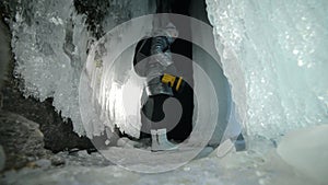 Travel woman on ice cave of Lake Baikal. Trip to winter island. Girl backpacker is walking of ice grot. Traveler looks