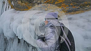 Travel of woman on ice of Lake Baikal. Trip to winter island. Girl is walking at foot of ice rocks. Traveler looks at