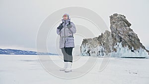 Travel of woman on ice of Lake Baikal. Trip to winter island. Girl is walking at foot of ice rocks. Traveler looks at