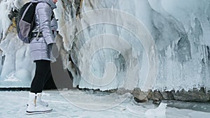 Travel of woman on ice of Lake Baikal. Trip to winter island. Girl is walking at foot of ice rocks. Traveler looks at