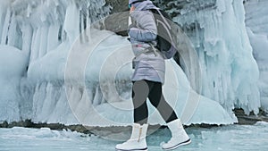 Travel of woman on ice of Lake Baikal. Trip to winter island. Girl is walking at foot of ice rocks. Traveler looks at