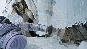 Travel of woman on ice of Lake Baikal. Trip to winter island. Girl is walking at foot of ice rocks. Traveler looks at