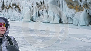 Travel of woman on ice of Lake Baikal. Trip to winter island. Girl is walking at foot of ice rocks. Traveler looks at