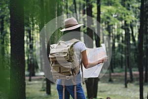 Travel woman reading map among trees at forest and searching directional for travling with a backpack