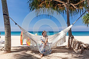 Travel Woman Sitting on White Hammock on Sandy Beach with Sea and Tropical Trees