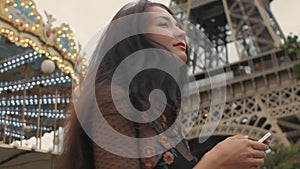 Travel woman using smartphone looking on map near the Eiffel tower and carousel, Paris.