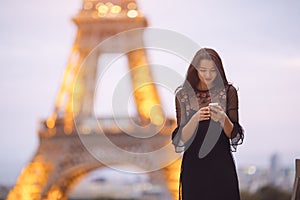 Travel woman using smartphone near the Eiffel tower and carousel, Paris. Evening little noisy image.