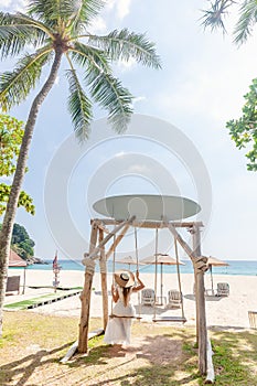 Travel Woman in White Dress and Straw Hat Sitting on Wooden Wings near Blue Sea