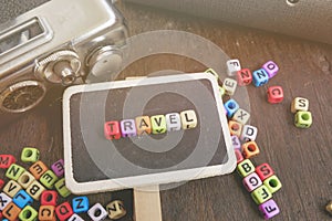 Travel word block, compass and vintage camera on wooden background