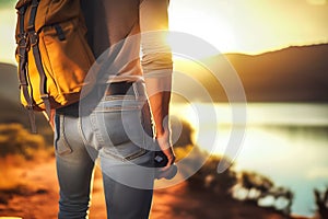 A traveler, adorned in blue jeans and a yellow backpack, stands by a serene lake, soaking in the beauty of a golden sunset