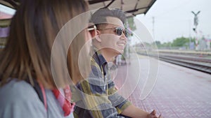 Traveler Asian backpack couple sitting on bench while waiting train, Young sweet couple tourist backpacker enjoy their journey in