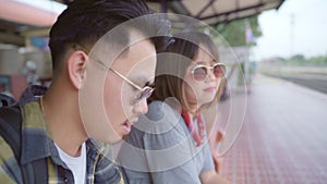 Traveler Asian backpack couple sitting on bench while waiting train, Young sweet couple tourist backpacker enjoy their journey in