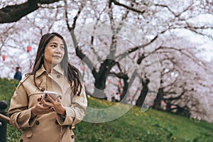 Traveler asian woman with mobile phone travel in sakura cherry blossom tree in Gongendo park Saitama Japan in spring season