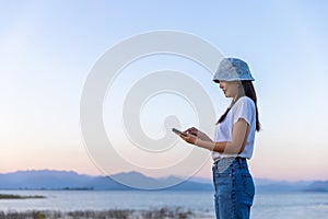 Traveler asian woman using mobile phone travel in lake at sunset in Phetchaburi Thailand