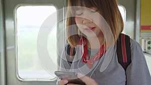 Traveler Asian woman using smartphone listening music relax while taking a train, Young female tourist backpacker enjoy her