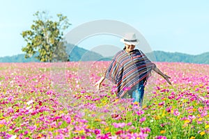 Traveler Asian women walking in the flower field and hand touch cosmos flower, freedom and relax in the flower meadow, blue sky ba