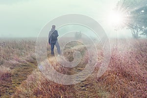 Traveler on autumn foggy meadow looks at on bright sunlight.