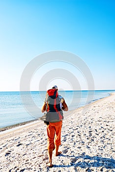 Traveler with backpack goes along the deserted beach