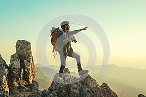 traveler with backpack and holding binocular standing on top of mountain pointing at view