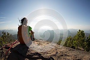 Traveler with backpack sit on the mountain peak rock observing locality