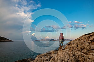 Traveler with backpack stands on the rock seashore