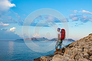Traveler with backpack stands on the rock seashore