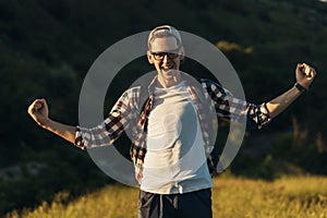 Traveler with a backpack stands in a winner pose with a raised hand on the top of a mountain, the concept of travel and recreation