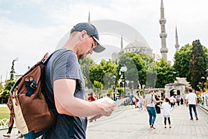 A traveler in a baseball cap with a backpack is looking at the map next to the blue mosque - the famous sight of