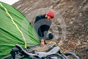 Traveler bearded male preparing his backpack for mountaineering. Image of young hiker man hiking in mountains with travel backpack