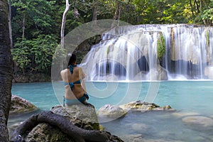 Traveler with blue swimsuit sit relax at Erawan Waterfall
