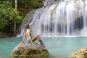 Traveler in blue swimsuit sit relax at Erawan Waterfall and natural