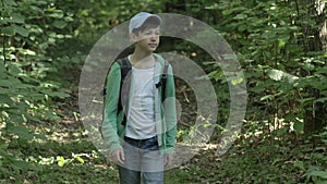 Traveler boy in a cap with a backpack walks through the woods and looks around