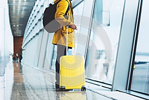 Traveler in bright jacket with yellow suitcase backpack at airport on background large window blue sky, passenger waiting flight