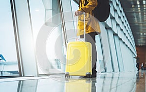 Traveler in bright jacket with yellow suitcase backpack at airport on background large window blue sky, passenger waiting flight