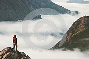 Traveler on cliff overlooking mountain clouds alone