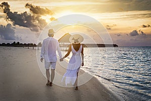 A traveler couple walks along a tropical beach during sunset time