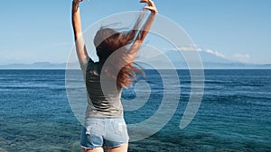 Traveler enjoys view of ocean, mountains. Girl hair flutters in wind, slow motion