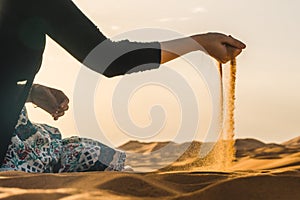 Traveler explorer girl sitting in the Sahara Desert and letting the sand fall from the hand, Morocco
