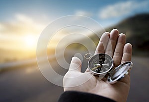 Traveler explorer man holding compass in a hand in mountains at sunrise, point of view
