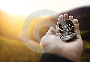 Traveler explorer man holding compass in a hand in mountains at sunrise, point of view