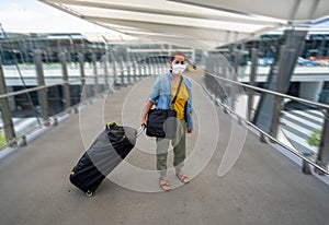 Traveler with face mask affected by coronavirus travel ban and COVID-19 pandemic flight restrictions