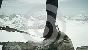 Traveler feet in leather shoe stomps on rock at snowy mountain scenic view