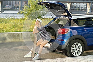 Traveler female relax leaning on longboard at car trunk. Woman resting after skateboarding outdoor